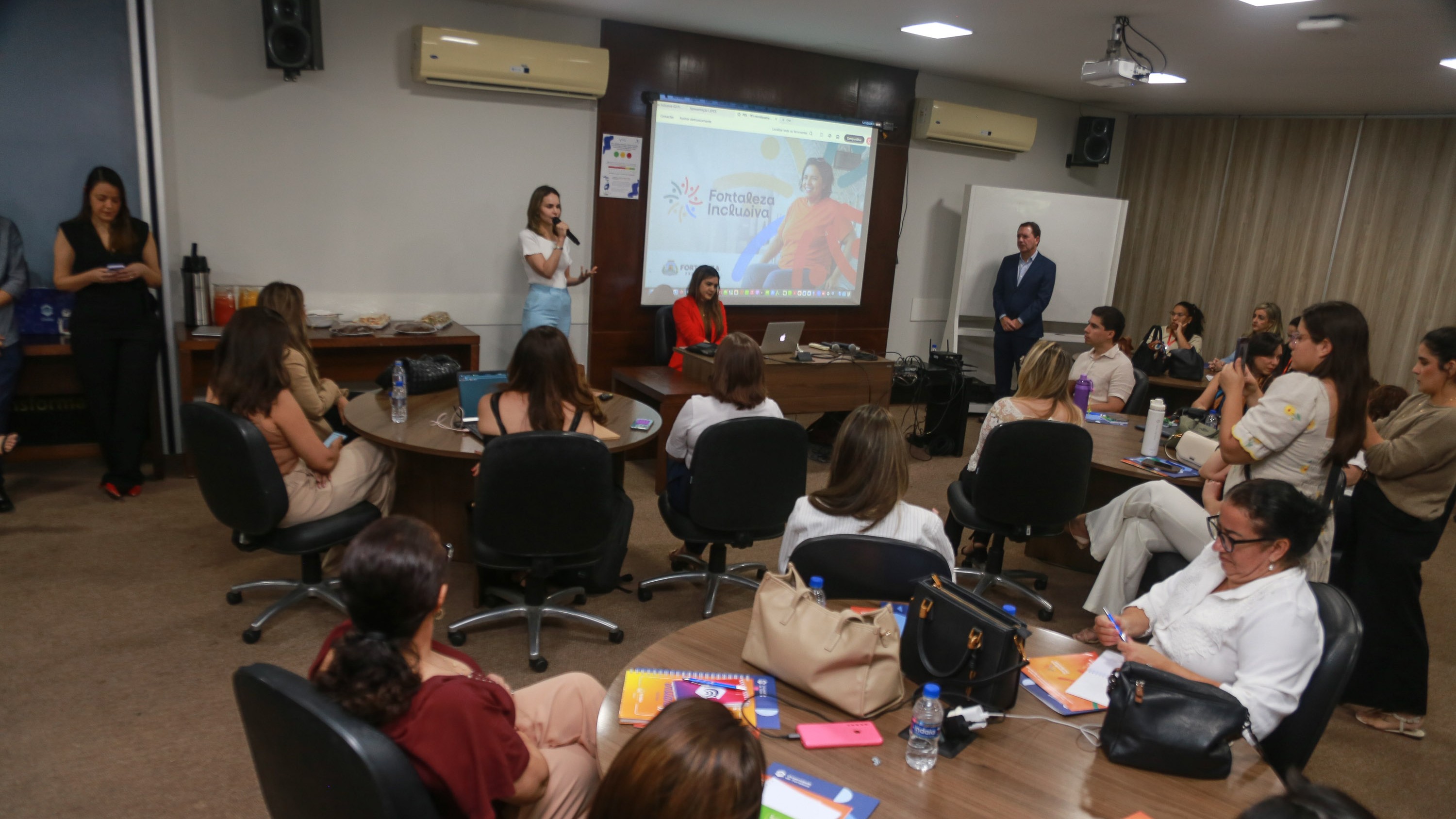 Gabriella Aguiar falar para um grupo de pessoas numa sala com telão